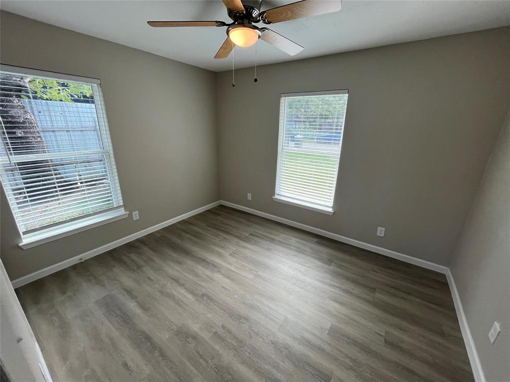 Neutral-toned interior space featuring wood-finish flooring, dual windows with horizontal blinds, and a central ceiling fan with an integrated light fixture