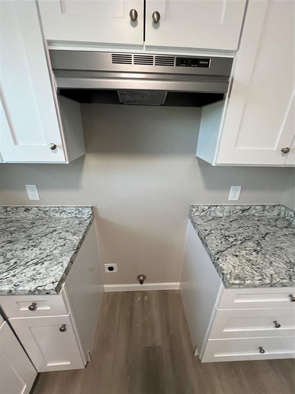 White shaker-style cabinetry, stone-patterned countertops, stainless steel range hood, and wood-finish flooring