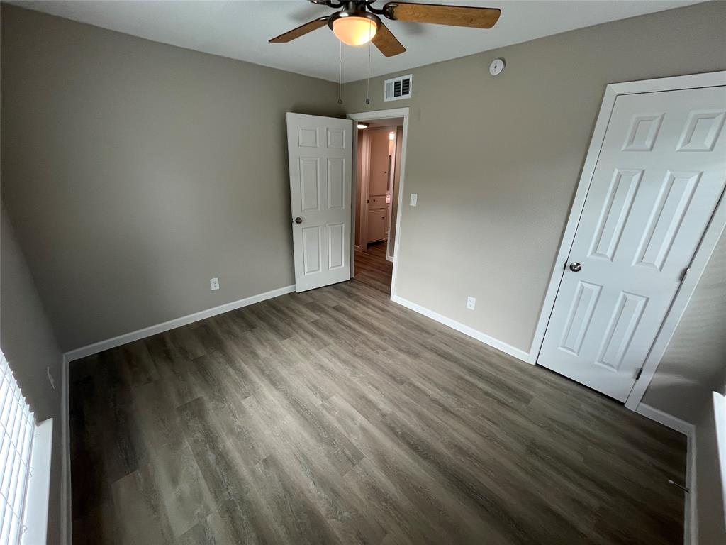 Neutral-toned interior room featuring wood-finish flooring, a ceiling-mounted light fixture with a fan, and two interior doors