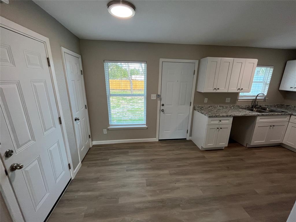 Kitchen featuring white shaker-style cabinetry, stone-patterned countertops, wood-finish flooring, and a stainless steel double-basin sink