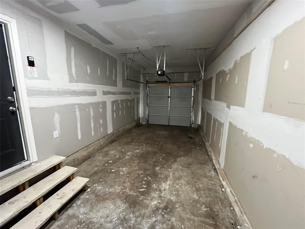 Single-vehicle garage featuring unfinished drywall, a concrete floor, an automated overhead door system, and wooden interior access steps