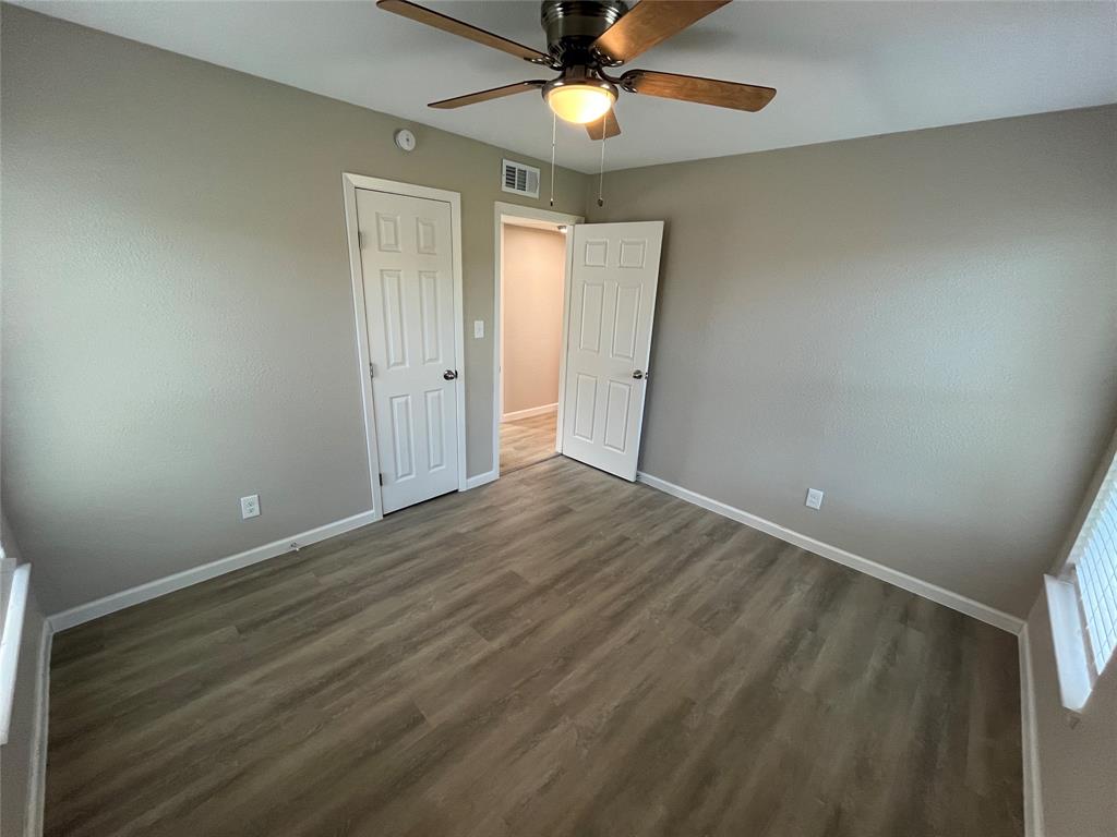 Neutral-toned room featuring wood-finish flooring, a ceiling-mounted light fixture with fan, and two six-panel interior doors