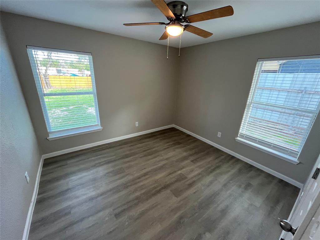 Neutral-toned interior featuring wood-finish flooring, dual windows with blinds, and a centrally mounted ceiling fan