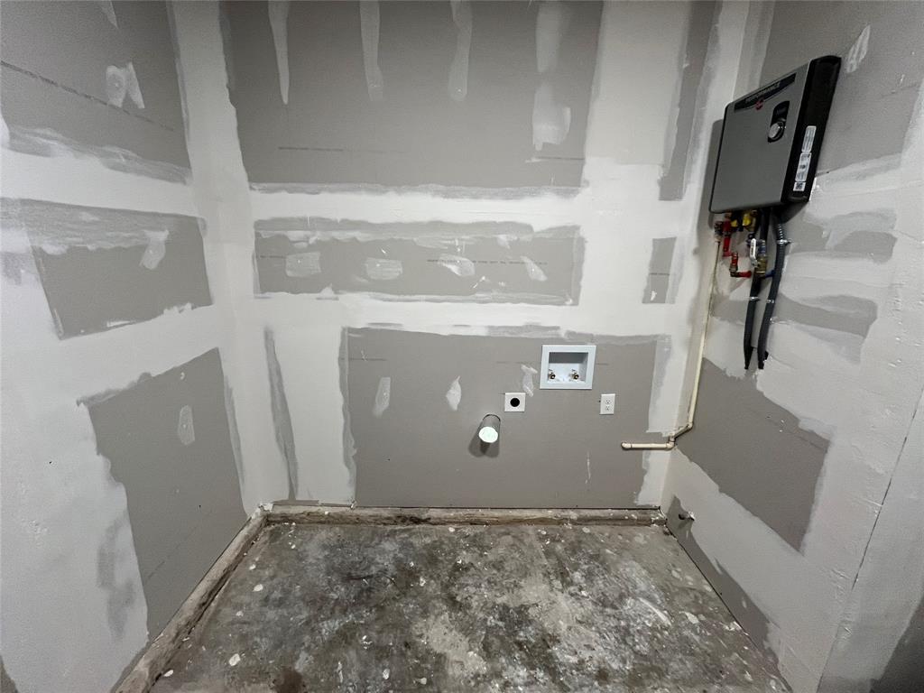 Utility area featuring unfinished drywall, a tankless water heater, and integrated plumbing hookups