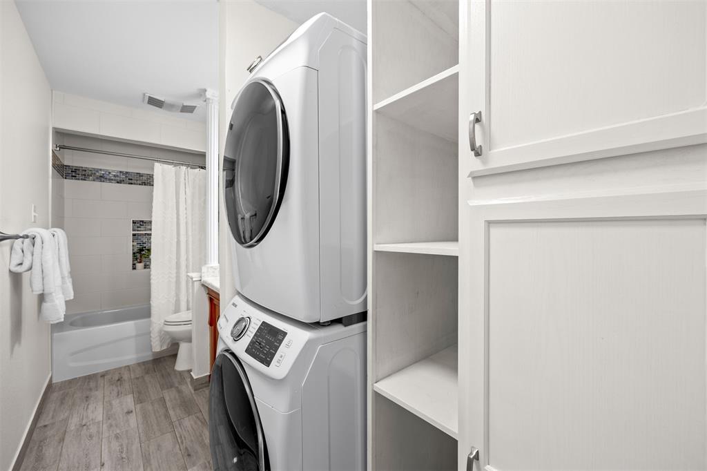 Dedicated laundry area with stacked appliances, white shaker-style cabinetry, and open shelving
