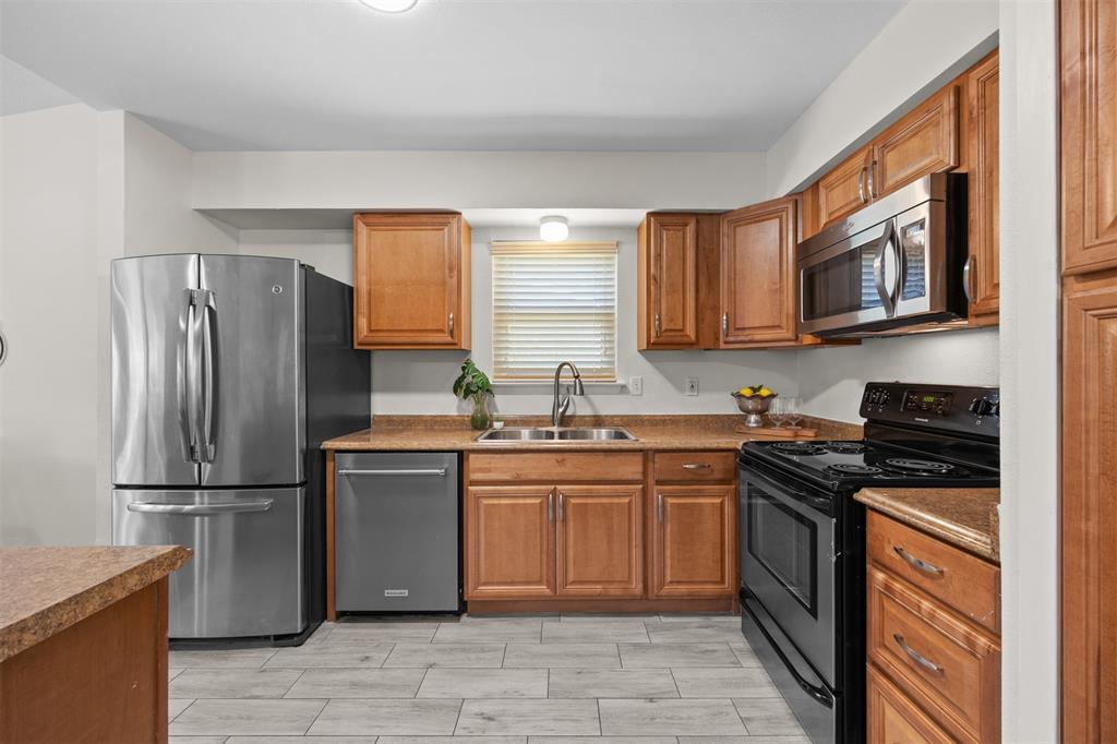 Kitchen featuring wood cabinetry, stainless steel appliances, a black range, a double basin sink, and wood-finish flooring