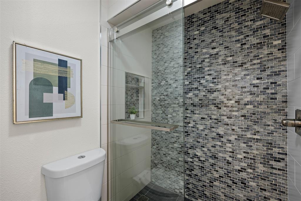 Glass-enclosed shower with mosaic tile surround, rainfall showerhead, and a fixed toilet