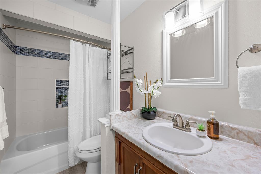Vanity with an integrated sink and light-toned countertop, wood-finish cabinetry, and a framed mirror with an overhead vanity light