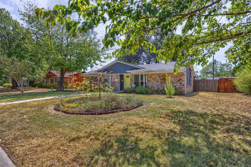 Brick exterior with a contrasting façade, a central landscaped garden bed, mature trees, and a privacy fence