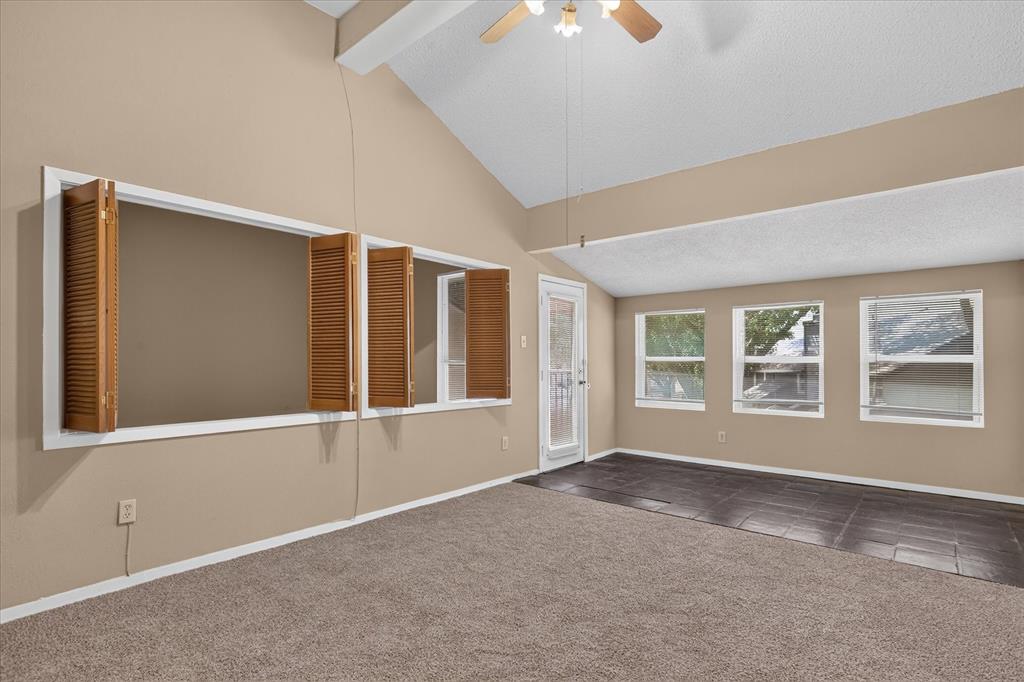 Vaulted ceiling with ceiling fan, large interior window with wood shutters, multiple exterior windows, tile flooring, and carpet flooring