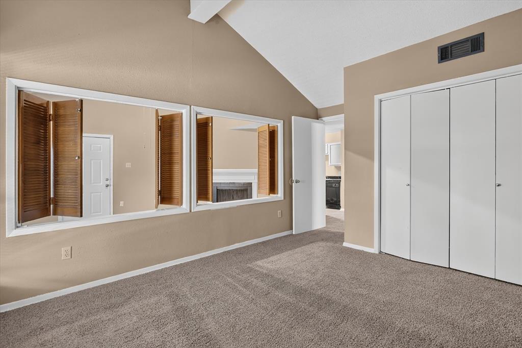 Vaulted ceiling, neutral tone walls, carpeted flooring, bi-fold closet doors, and interior shutters