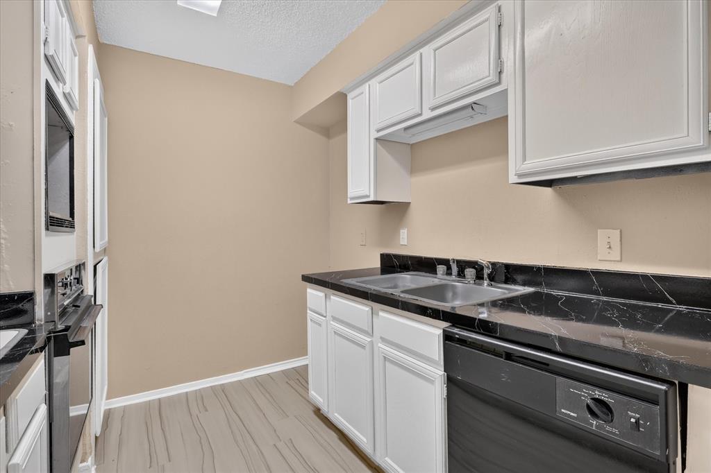 Kitchen featuring wood-finish flooring, white cabinetry, a double basin sink, black countertops, and a built-in oven and microwave