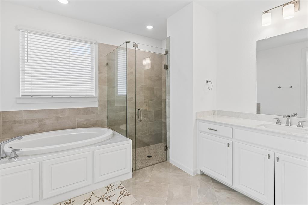 Soaking tub with white cabinetry, glass-enclosed shower, dual vanity with undermount sinks, and tile flooring