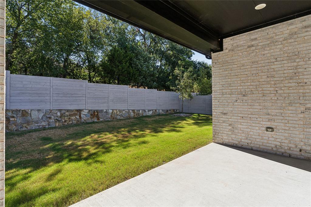 Concrete patio with a light-colored brick exterior wall, black overhang, and recessed lighting