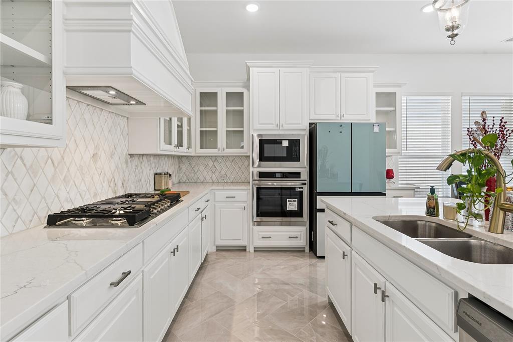 White cabinetry with glass-front accents, stainless steel built-in appliances, a gas cooktop, and a double basin sink