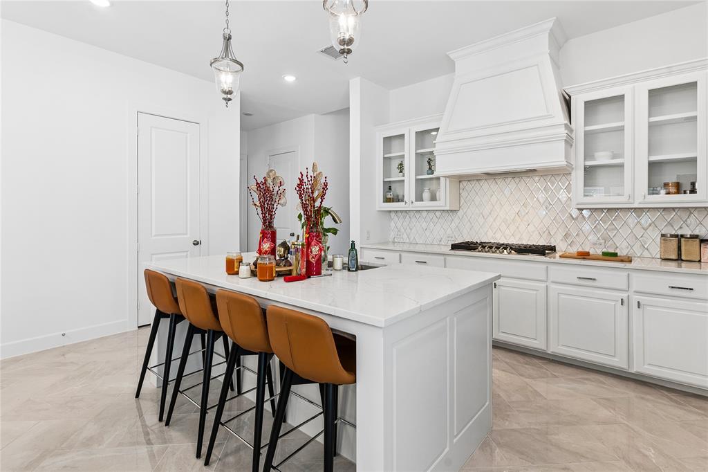 Kitchen featuring a large island with seating, white shaker-style cabinetry, a decorative range hood, a gas cooktop, and a diamond-patterned tile backsplash