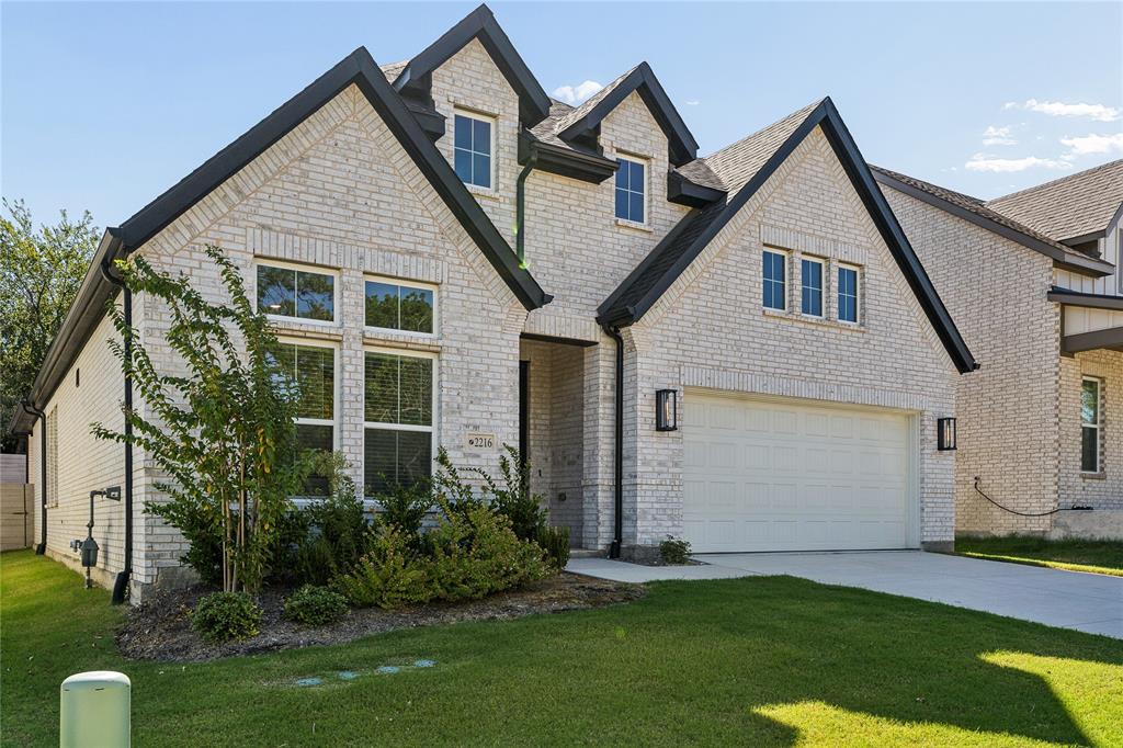 Light-colored brick exterior with dark trim accents, multiple gables, an attached garage, a concrete driveway, and landscaping