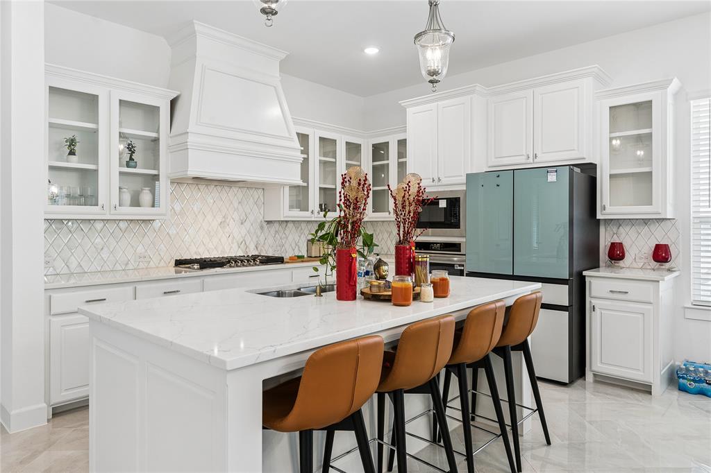 White cabinetry with glass-front display uppers, quartz countertops, a diamond-patterned tile backsplash, and a large center island