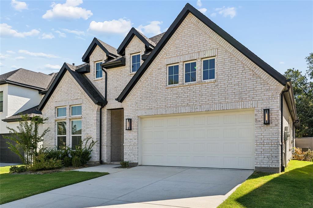 Light-colored brick exterior with dark trim accents, multiple gables, a two-car garage, and a concrete driveway