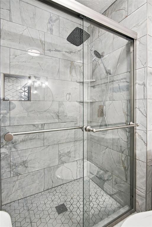 Glass-enclosed shower with a rainfall showerhead, handheld sprayer, geometric tile flooring, and large format wall tiling