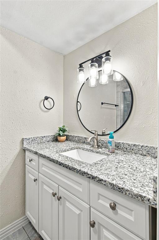 White vanity with paneled doors, speckled countertop, undermount sink, and brushed nickel faucet