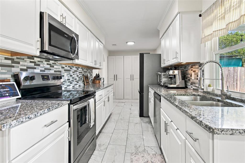 Galley kitchen featuring white cabinetry, granite-finish countertops, mosaic tile backsplash, and stainless steel appliances