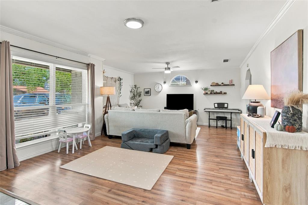 Wood-finish flooring, white walls, crown molding, a large window with blinds, and recessed lighting fixtures Wood-finish flooring, white walls, crown molding, a large window with blinds, and recessed lighting fixtures