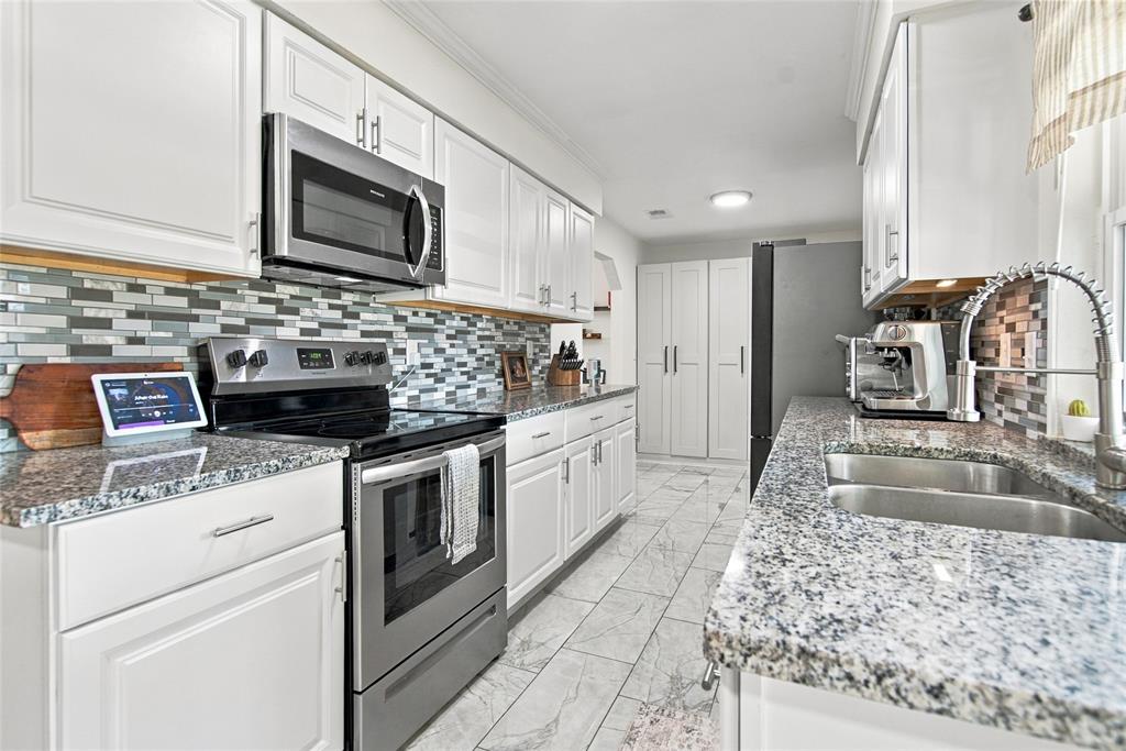 White cabinetry, stainless steel appliances, mosaic tile backsplash, double basin sink, and stone-finish countertops