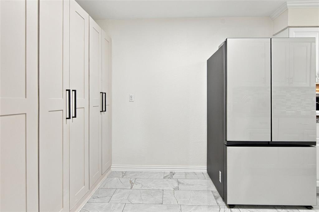 Full-height cabinetry with matte black hardware, contemporary refrigerator with a black side panel, white walls, and light-toned tile flooring