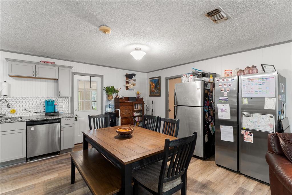 Kitchen area featuring gray cabinetry, stone-finish countertops, a hexagonal tile backsplash, stainless steel appliances, and wood-finish flooring