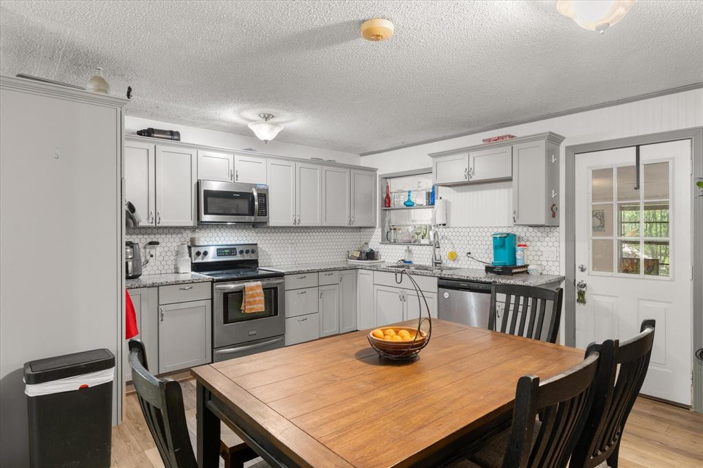 Kitchen featuring  shaker cabinetry, stainless steel appliances, speckled stone-finish countertops, and a white hexagonal tile backsplash