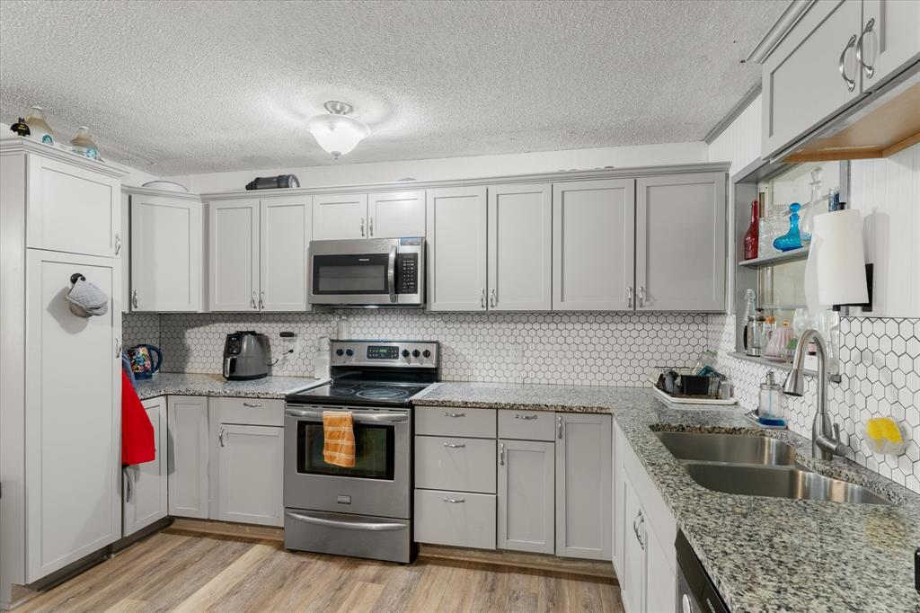 Kitchen featuring  stone-finish countertops, stainless steel appliances, a white hexagonal tile backsplash, and wood-finish flooring