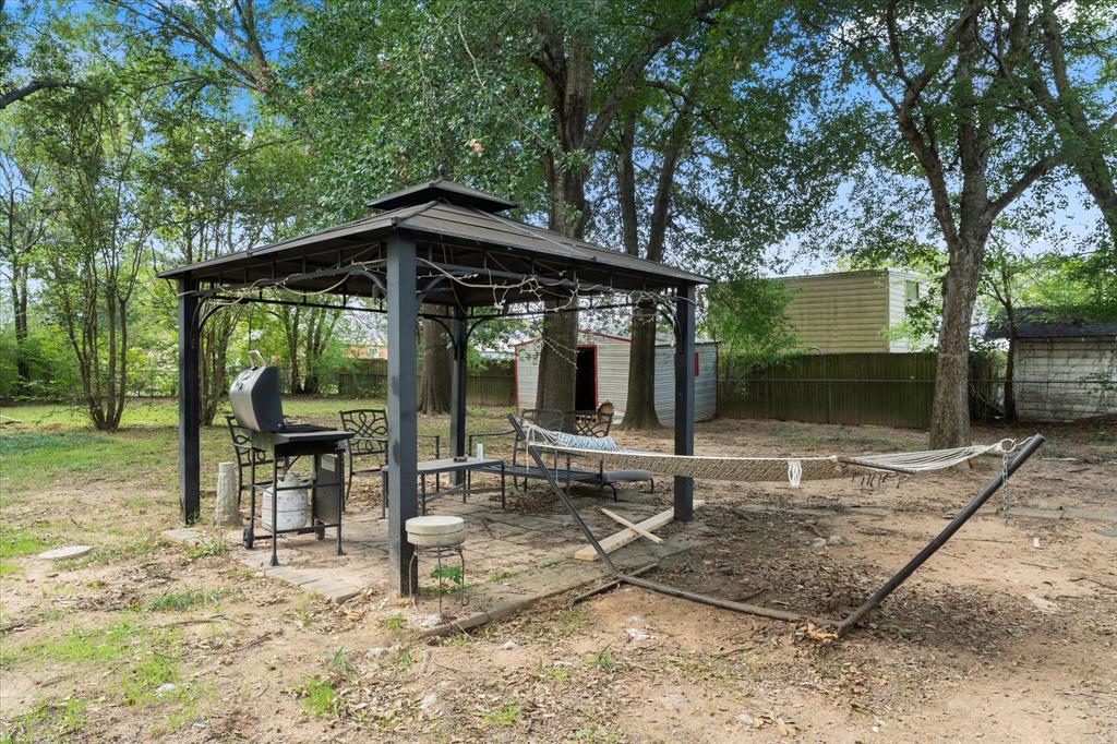 Outdoor space featuring a metal-framed gazebo with a peaked roof, concrete patio, and mature trees