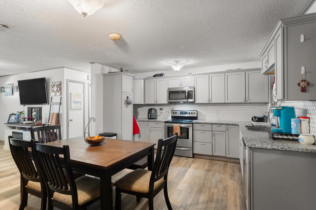 Kitchen featuring grey cabinetry, stone-finish countertops, stainless steel appliances, hexagonal tile backsplash, and wood-finish flooring