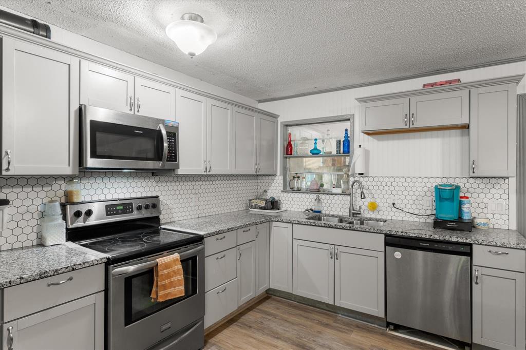 Remodeled Kitchen featuring shaker-style cabinetry, stone-finish countertops, stainless steel appliances, a hexagonal tile backsplash, and wood-finish flooring