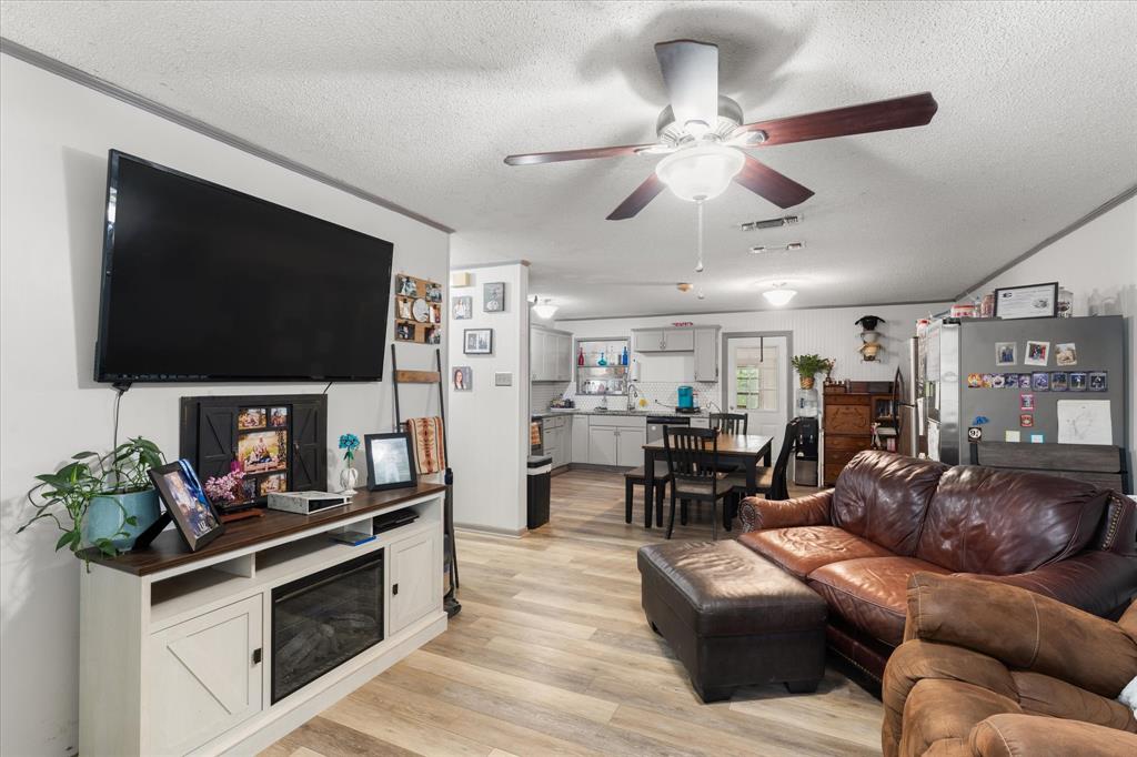 Open-concept living space featuring wood-finish flooring, ceiling fan with integrated lighting, and built-in electric fireplace console