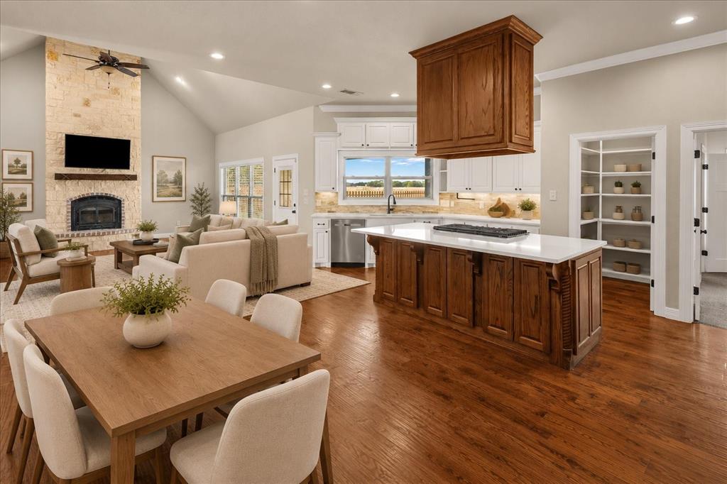 Vaulted ceilings, wood-finish flooring, stone-clad fireplace with mantel, kitchen island with built-in gas cooktop, and built-in shelving