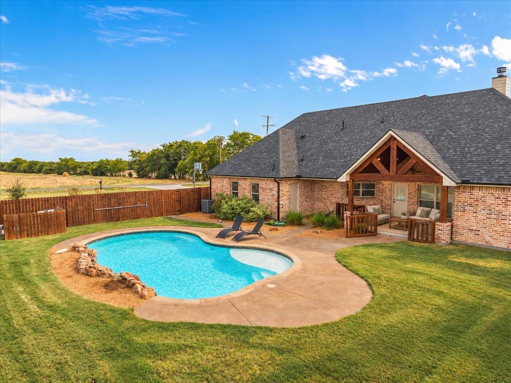 Brick exterior with a gabled roofline, a built-in covered patio, and a fenced backyard featuring a swimming pool with concrete decking