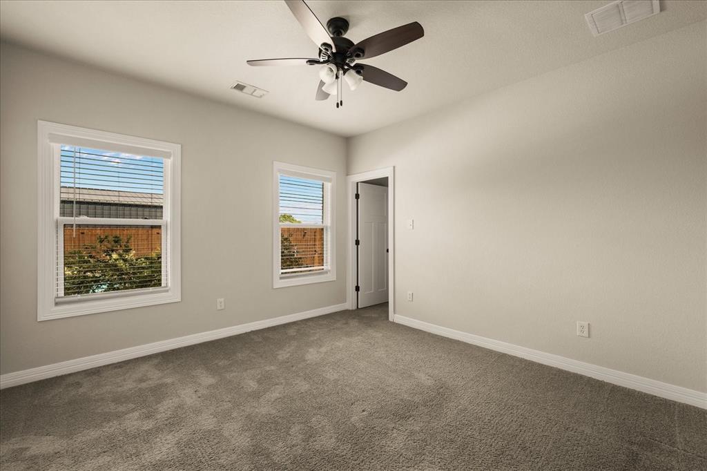 Spacious room featuring neutral carpeting, two double-hung windows with blinds, a ceiling fan with integrated lighting, and a white interior door