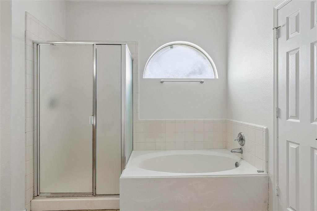 Built-in soaking tub with chrome fixtures, tiled surround, and frosted arch window