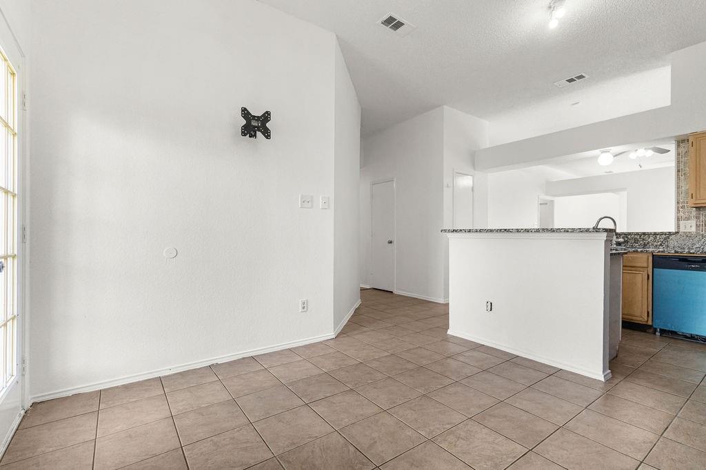 Ceramic tile flooring, vaulted ceilings, and kitchen peninsula featuring a stone-look countertop