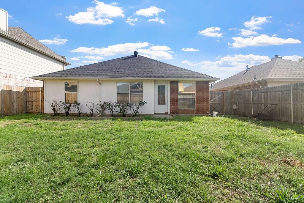 Rear exterior featuring a brick and stucco facade, a hip roof, and a fenced-in grass backyard