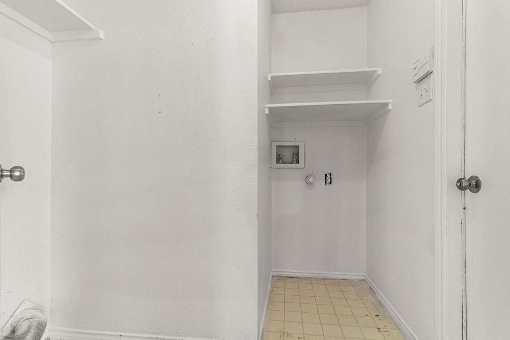 Utility space featuring recessed wall-mounted utility connections, dual open built-in shelves, and tile flooring