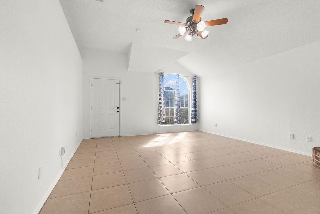 Vaulted ceiling with an arched window, tile flooring, and a ceiling fan with integrated lighting
