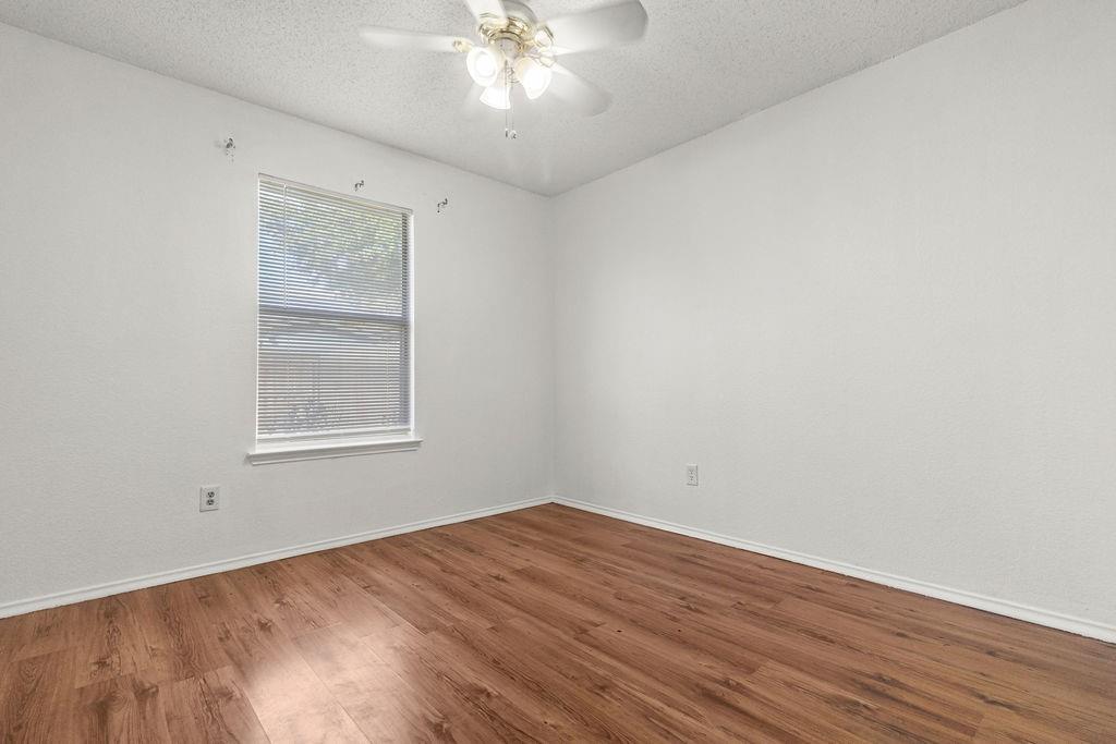 Room featuring wood-finish flooring, a neutral color palette, a window with horizontal blinds, and a ceiling-mounted light fixture with an integrated fan