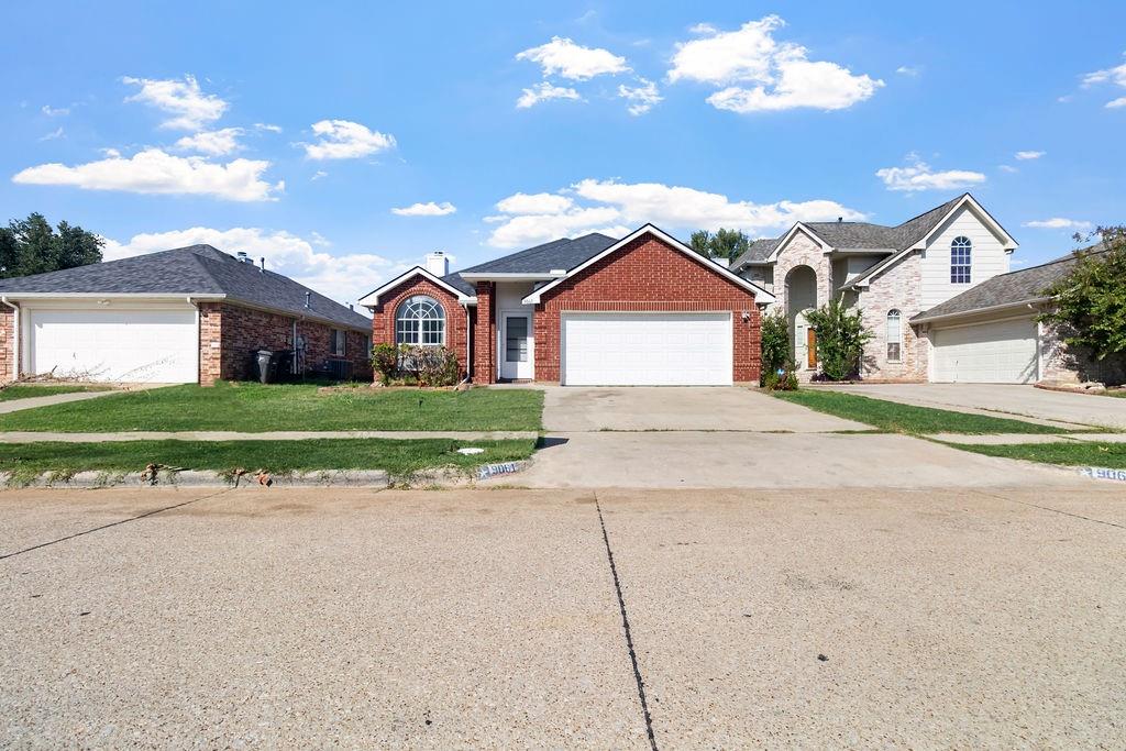 Red brick exterior featuring a front-facing attached two-car garage, arched window accents, and a concrete driveway