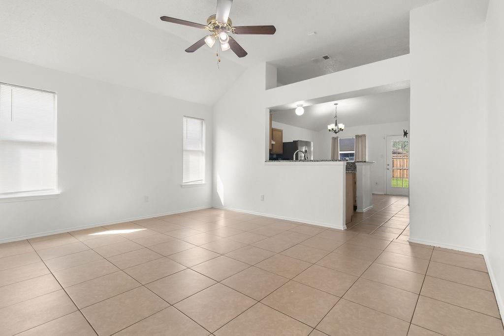 Vaulted ceilings, large-format ceramic tile flooring, ceiling fan with integrated lighting, and a breakfast bar counter