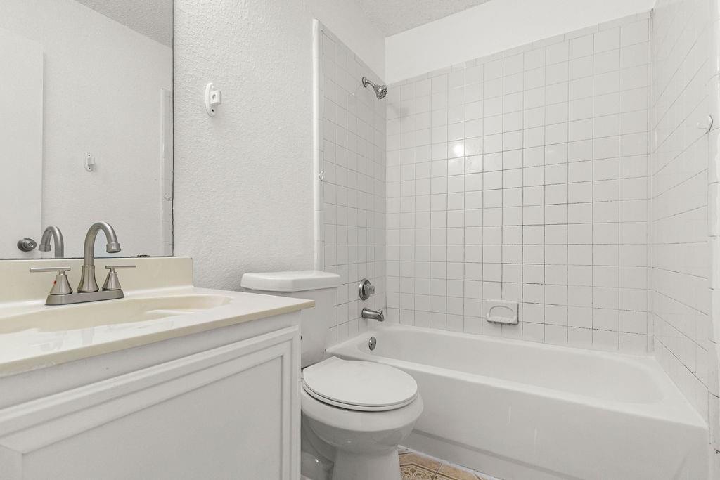Bathroom featuring a white vanity with an integrated countertop sink, polished chrome faucet, full-width mirror, and a shower-tub combination with white tile surround