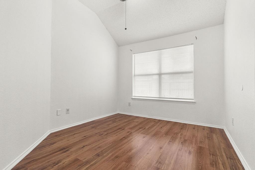 Room featuring wood-finish flooring, a vaulted ceiling, and a large window with horizontal blinds
