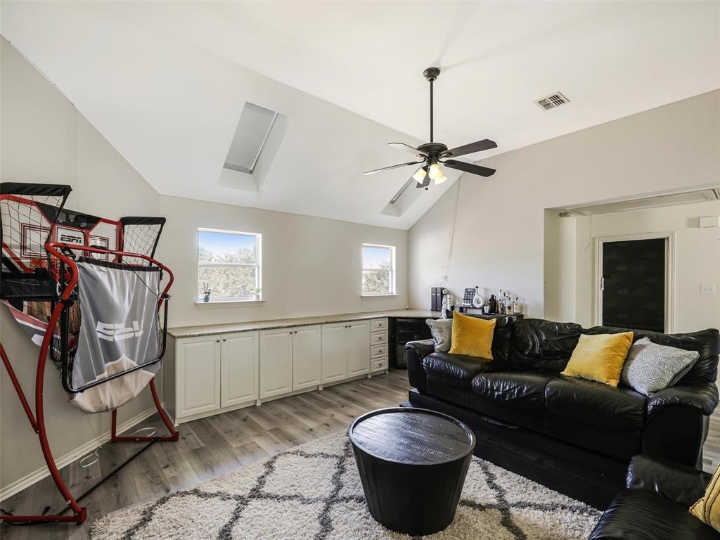 Vaulted ceiling with skylight, wood-finish flooring, ceiling fan, and built-in white cabinetry with a light-toned countertop